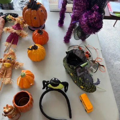 Sale Photo Thumbnail #191: Assortment of Halloween decorations, including a purple tinsel cat, ceramic pumpkins, scarecrow figures, a witch's boot, and a spider headband.