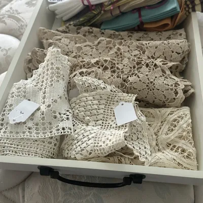 Sale Photo Thumbnail #130: Assorted vintage linens, including crocheted lace doilies and runners, alongside folded cloth napkins in a white wooden tray.