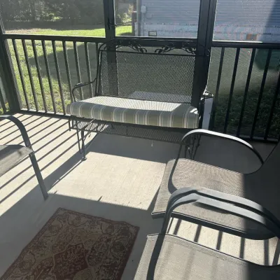 Sale Photo Thumbnail #172: Black wrought iron patio glider bench with a striped cushion, shown alongside mesh-backed patio chairs on a screened-in porch.