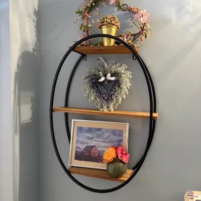 Sale Photo Thumbnail #68: Oval black metal wall shelf with three wooden tiers, decorated with floral wreaths, a framed picture, and small potted plants.