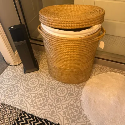 Sale Photo Thumbnail #139: Large woven wicker laundry hamper with a matching lid and white fabric liner, shown alongside a Lasko tower fan.