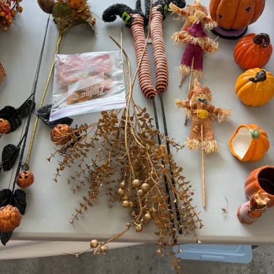 Sale Photo Thumbnail #190: Assortment of autumn and Halloween decorations, featuring witch leg yard stakes, small scarecrow picks, faux gold foliage, and decorative pumpkins.