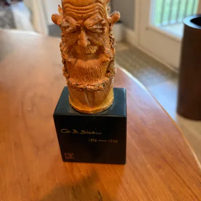 Sale Photo Thumbnail #57: Carved bamboo root bust of George Bernard Shaw, mounted on a black pedestal base inscribed with his name and lifespan (1856-1950).