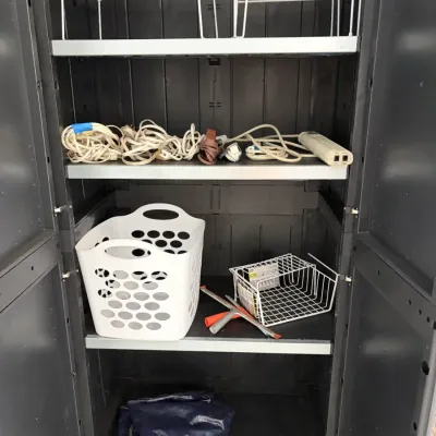 Sale Photo Thumbnail #150: Black plastic utility storage cabinet with four shelves, containing various household items including wire shelf risers, extension cords, a white plastic basket, and a squeegee.