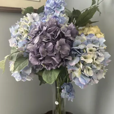 Sale Photo Thumbnail #73: Faux hydrangea floral arrangement featuring purple, blue, and cream blossoms in a tall, clear glass cylinder vase.