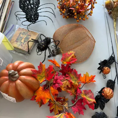 Sale Photo Thumbnail #192: Assortment of autumn and Halloween decorations, featuring a faux pumpkin, colorful leaf garland, glittery black spiders, and wire mesh pumpkin accents.