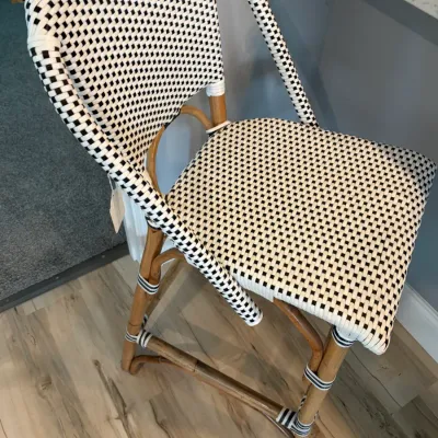 Sale Photo Thumbnail #89: French bistro-style counter stool featuring a black and white woven checkered seat and backrest on a natural rattan frame.