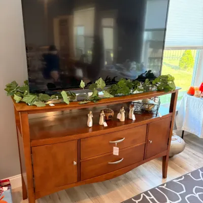 Sale Photo Thumbnail #81: Contemporary wooden media console with a warm cherry finish, featuring two drawers, two side cabinets, and an open shelf, topped with a large flat-screen television.