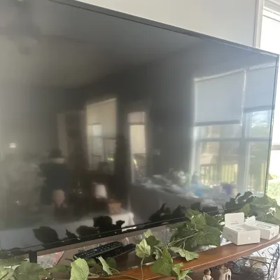 Sale Photo Thumbnail #70: Large flat-screen television with a thin black bezel, shown with two remote controls and boxed Apple AirPods Pro on the stand below.