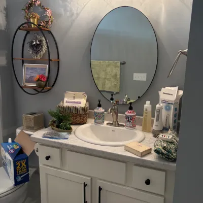 Sale Photo Thumbnail #158: Modern white bathroom vanity with a faux-marble countertop, paired with an oval black-framed wall mirror and a three-light glass vanity fixture.