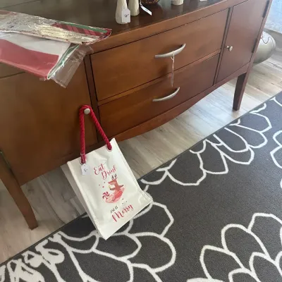 Sale Photo Thumbnail #82: Mid-century modern style wooden sideboard featuring curved drawers with silver-tone pulls, styled with Willow Tree angel figurines and a festive tote bag.