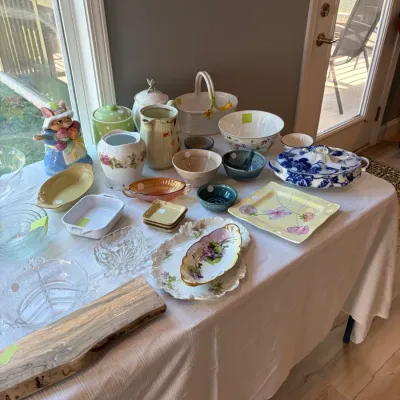 Sale Photo Thumbnail #110: Assortment of vintage and decorative tableware, featuring a blue and white transferware tureen, floral ceramic platters, glass bowls, and a live-edge wooden serving board.