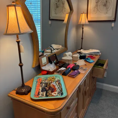 Sale Photo Thumbnail #121: Vintage light wood dresser with a matching arched mirror, displaying a variety of costume jewelry, small storage boxes, and a pair of slender buffet lamps.