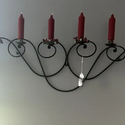Sale Photo Thumbnail #61: Wrought iron wall-mounted candelabra featuring scrollwork details, holding six red ribbed taper candles with decorative bobeches.