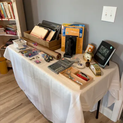 Sale Photo Thumbnail #163: Assorted office supplies and desk accessories, including file folders, a calculator, scissors, and several vintage and modern desk clocks, displayed on a table.