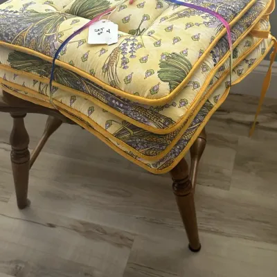 Sale Photo Thumbnail #126: Set of four yellow and purple floral patterned chair cushions with ties, bundled together on a wooden chair.
