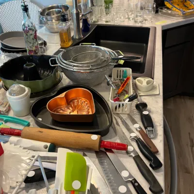 Sale Photo Thumbnail #112: Collection of kitchen utensils and baking supplies, including a wooden rolling pin, various kitchen knives, a heart-shaped copper mold, and stainless steel colanders.