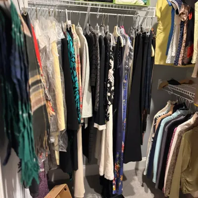 Sale Photo Thumbnail #43: Assortment of women's contemporary clothing, including dresses, sweaters, and outerwear, hanging on closet racks alongside a selection of shoes and accessories on the floor.