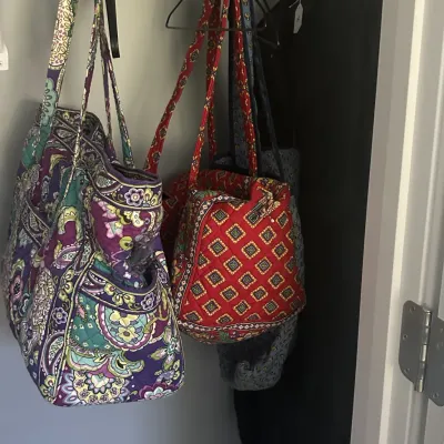 Sale Photo Thumbnail #48: Assorted Vera Bradley quilted cotton handbags, including a purple and teal paisley tote and a red geometric patterned shoulder bag, hanging in a closet.
