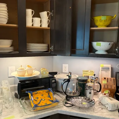 Sale Photo Thumbnail #114: Assorted kitchenware and small appliances, including white ceramic dinnerware, a yellow colander, a toaster oven, a slow cooker, and various coffee accessories.