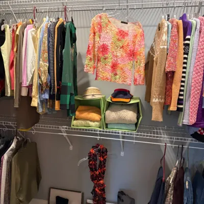 Sale Photo Thumbnail #44: Assorted women's clothing and accessories, featuring knit sweaters, a textured floral top, and various boots and shoes organized on wire closet shelving.