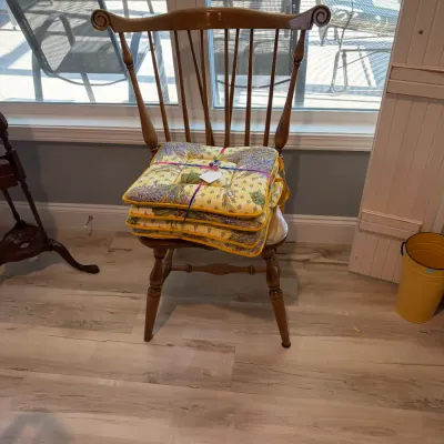 Sale Photo Thumbnail #94: Traditional wooden Windsor-style dining chair with a high spindle back and scrolled top rail, holding a stack of four yellow and purple floral-patterned seat cushions.