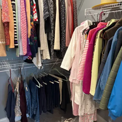 Sale Photo Thumbnail #45: A selection of women's clothing including sweaters, jackets, pants, and robes hanging in a closet, alongside various shoes and slippers on the floor.