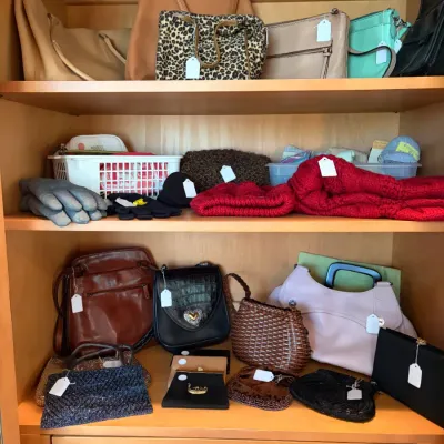 Sale Photo Thumbnail #41: Collection of assorted women's handbags, evening clutches, and winter accessories like knit hats and gloves displayed on wooden shelves.