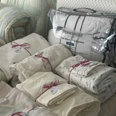 Sale Photo Thumbnail #127: Assortment of bedding and linens, including a new-in-package Berkshire Life queen-size down alternative blanket, lace tablecloths, and various folded sheet sets tied with pink ribbon.