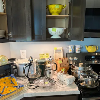 Sale Photo Thumbnail #113: An assortment of kitchenware and small appliances, including a slow cooker, hand mixer, stainless steel pots, and colorful enamel colanders.