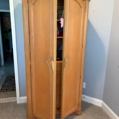 Sale Photo Thumbnail #95: French Provincial style light wood armoire featuring a carved shell crest, fluted side columns, and double doors opening to interior storage.
