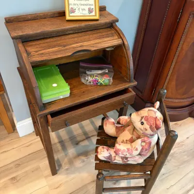 Sale Photo Thumbnail #85: Vintage child-sized wooden roll-top desk with a single drawer, paired with a matching wooden chair featuring a floral fabric teddy bear.