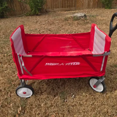 Sale Photo Thumbnail #217: A classic red Radio Flyer folding wagon featuring a durable fabric body, sturdy metal frame, and a pull handle. Designed for easy storage and transport. Shows some light outdoor wear and minor staining on the interior fabric, but remains in good, function
