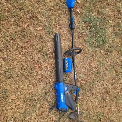 Sale Photo Thumbnail #214: A Kobalt 40V Max cordless outdoor power equipment set. Includes a handheld leaf blower, a string trimmer/edger, and one Kobalt 40V Max lithium-ion battery. The items show signs of outdoor use, including dirt and grass residue on the trimmer head, but appe