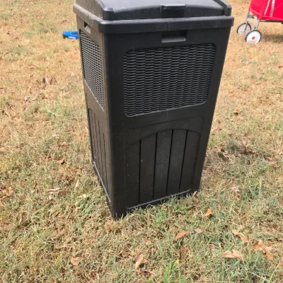 Sale Photo Thumbnail #213: A black resin outdoor trash can featuring a decorative faux-wicker weave pattern on the front and sides. Designed with a hinged lid and latch to keep contents secure. Shows some light outdoor wear and dust from storage, but is in overall good, functional 