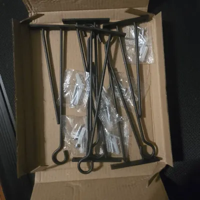 Sale Photo Thumbnail #185: A set of black metal wall brackets, likely for shelves or hanging items, featuring a minimalist design with a looped end. Includes several sealed packets of mounting screws and drywall anchors. Appears unused and in excellent condition, stored in its orig