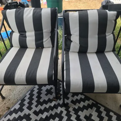 Sale Photo Thumbnail #209: A pair of outdoor patio armchairs featuring sturdy black metal frames and thick, comfortable cushions with bold black and white vertical stripes. The chairs show some light outdoor wear and minor dust from use, but remain in sturdy, functional condition.