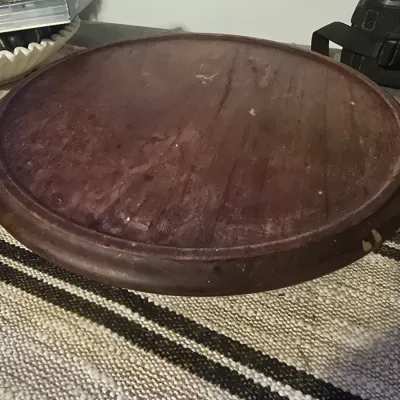 Sale Photo Thumbnail #191: A circular wooden display stand or base with a routed, beveled edge. Features a dark brown finish showing natural wood grain. Shows some surface wear, scuffs, and minor paint specks consistent with age and use. Ideal for displaying sculptures, vases, or o