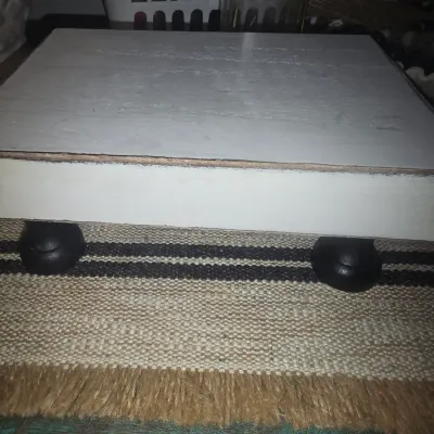 Sale Photo Thumbnail #197: 8x6x3 rectangular wooden display riser or decorative stand painted in a distressed white finish. Features four rounded black feet. Ideal for farmhouse or rustic home decor to elevate plants, candles, or other decorative accents. Shows minor wear and distr