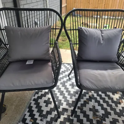 Sale Photo Thumbnail #208: A pair of contemporary outdoor patio chairs featuring black woven resin wicker/cord frames on metal legs. Includes matching grey seat cushions and back pillows. Showing light signs of outdoor use and minor weathering, but overall in good, sturdy condition