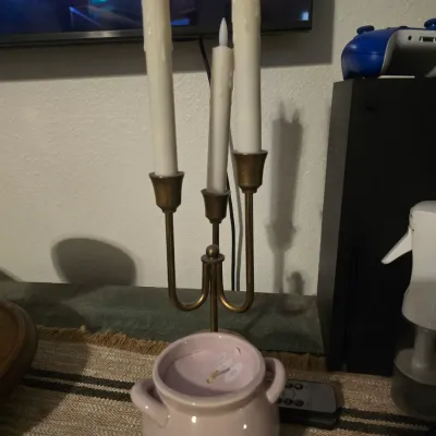 Sale Photo Thumbnail #186: A decorative brass-tone metal three-light candelabra paired with three white plastic LED taper candles featuring faux wax drips. Also includes a small pink ceramic cauldron-style candle with handles and feet. Items show light wear from use.