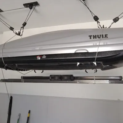 Thule rooftop cargo carrier in silver and black, suspended from a garage ceiling pulley storage system.