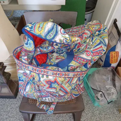 Vera Bradley quilted cotton duffel bag in a vibrant, multi-colored paisley pattern, resting on a small wooden chair with a cane seat.