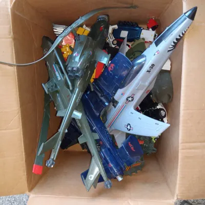 Cardboard box filled with vintage 1980s G.I. Joe vehicles, including the Conquest X-30 jet, Cobra Rattler, and Dragonfly helicopter.