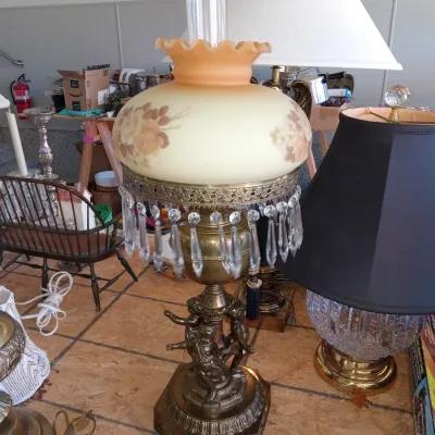 Vintage hurricane-style table lamp featuring a brass base with cherub figures, hanging crystal prisms, and a hand-painted floral glass...