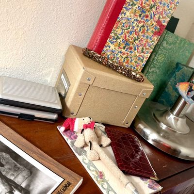 Sale Photo Thumbnail #80: Assorted desk accessories including a small cardboard storage box, a silver-toned card case, a decorative pen, and a small plush bear pen on a wooden surface.