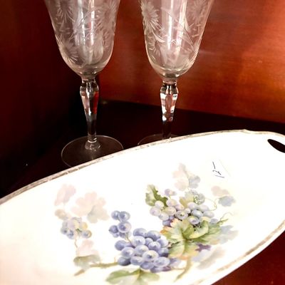 Sale Photo Thumbnail #104: Pair of vintage etched crystal wine glasses with floral motifs, shown alongside a hand-painted porcelain serving dish featuring a grape design.