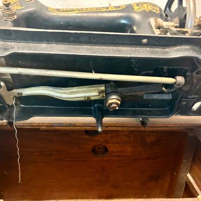 Sale Photo Thumbnail #67: Underside mechanism of an antique Minnesota A treadle sewing machine, showing the metal gears and drive rod inside its wooden cabinet.