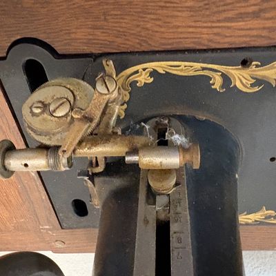 Sale Photo Thumbnail #69: Vintage Singer sewing machine bobbin winder attachment, showing some dust and wear, mounted on a black cast iron body with gold filigree details.
