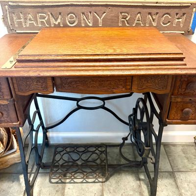 Sale Photo Thumbnail #71: Antique treadle sewing machine base with a wooden cabinet top featuring carved drawers, shown with a rustic wooden "Harmony Ranch" sign.